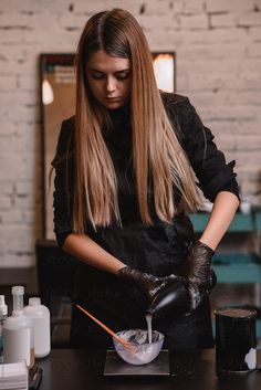 a woman with long hair and black gloves is mixing something in a bowl on a table