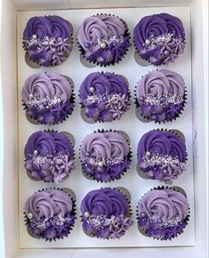 twelve cupcakes with purple frosting and silver decorations in a white cardboard box