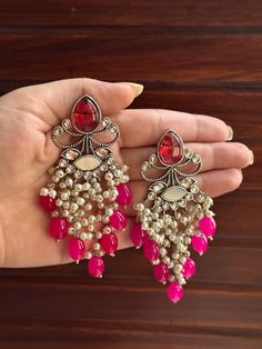 High quality handmade earrings with a lovely pop of pink that is sure to make a statement! These earrings look cute and classy at the same time and can be used at a number of occasions because of their silver detailing. They are also light weight and easy to wear!  For any queries, please feel free to contact us. Happy shopping! Hot Pink Earrings, Lehenga Designs Simple, Heavy Earrings, Dangler Earrings, Birthday Cake Chocolate, Pink Saree, Lehenga Designs, White Earrings, Antique Earrings