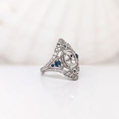 This gorgeous Edwardian style ring semi mount would make a stunning engagement or statement ring! Accented with natural earth mined diamonds and blue sapphires, beautiful metal work and milgrain detailing gives this piece an elegant charm. Which gemstone would you set in this exquisite piece of jewelry?  Specifications Item Type: Ring Semi Mount Head size: 8x6mm Shape: Oval Metal: 14k/4.838g Diamond Clarity/Color: SI / G-H Diamond Count/Weight: 54/0.81 cttw Blue Diffused Sapphire Count/Weight: 6 I'm Single, Designer Silver Jewellery, Edwardian Style, Jewelry Showcases, Ring Setting, Edwardian Fashion, Metal Work, 14k Gold Ring, Wedding Board