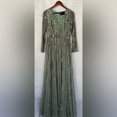 a green dress hanging on a wall with a hanger in front of it that has sequins all over it