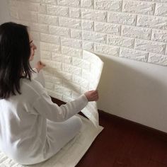 a woman is painting a brick wall with white paint and she has her hands on the edge of the board