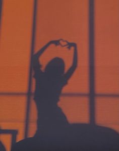 the shadow of a person holding a heart shaped object in front of a large window