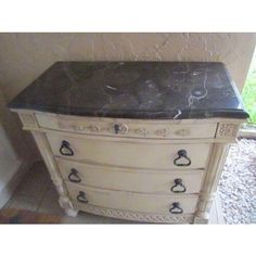 an old dresser with black marble top and drawer pulls on the bottom, in front of a window