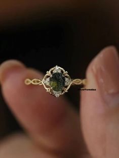 a close up of a person's hand holding a ring with a green stone in it