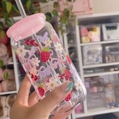 a person holding up a cup with strawberries and flowers on it in front of shelves