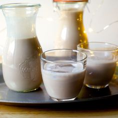 three glasses filled with liquid sitting on top of a metal tray next to jugs