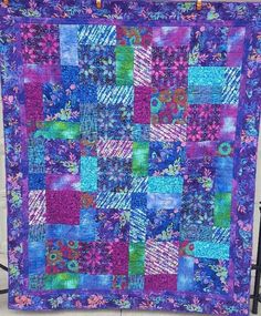 a purple and blue quilt hanging on a wall