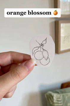 someone is holding up a piece of paper with an orange blossom drawn on it in the shape of a heart