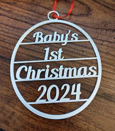 a baby's 1st christmas ornament hanging on a wooden table with a red ribbon