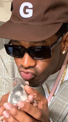 a man wearing sunglasses and a hat holding a small bird in his right hand while looking at the camera