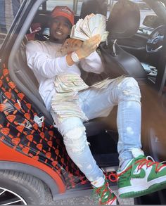 a man sitting in the passenger seat of a car holding money and wearing green sneakers