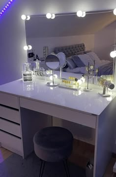 a white vanity with lights on it and a stool in front of the mirror that is lit up