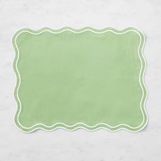 a green place mat on a white surface with an empty square in the middle and a scalloped edge