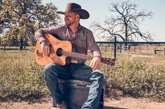 a man with a cowboy hat sitting on a suitcase holding an acoustic guitar in his hands