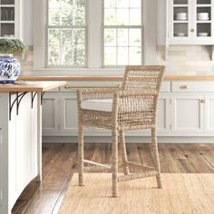 a wicker bar stool sits in the middle of a kitchen with white cabinets and wood floors