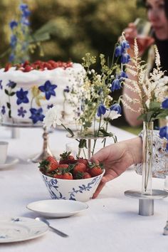 a table topped with plates and vases filled with strawberries next to cake covered in blue flowers