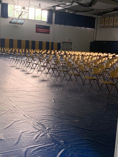 an empty room with rows of chairs covered in blue tarp and yellow folding chairs