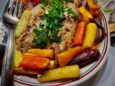 a white plate topped with meat and veggies next to a knife and fork