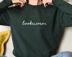 a woman sitting on the floor with her hands behind her head wearing a green sweatshirt that says lookwork