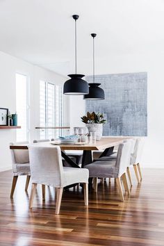 a dining room table with white chairs and black lamps