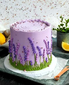 a purple cake decorated with lavender flowers and green grass on a tray next to lemons