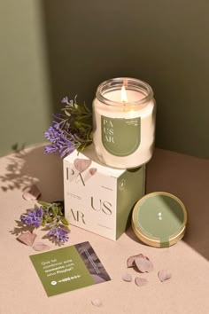 a candle sitting on top of a table next to a box and some purple flowers