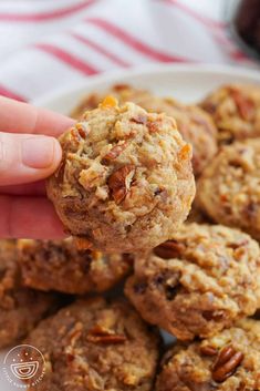 a person is holding a cookie in front of a plate full of oatmeal cookies