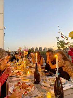 a group of people sitting at a table eating food and drinking wine with candles in front of them