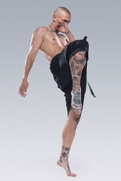 a man with tattoos on his arms and legs is doing a kickbox pose in front of a gray background