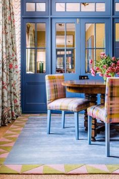 a dining room with blue walls and colorful chairs in front of a table that has flowers on it