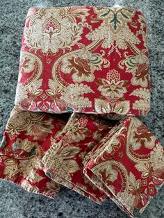 four red and gold paisley print napkins on a gray countertop next to each other