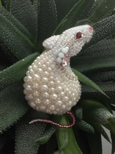 a white beaded mouse sitting on top of a green leafy plant with red eyes