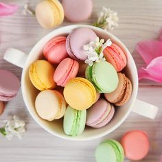 colorful macaroons are in a white bowl on a table with pink tulips