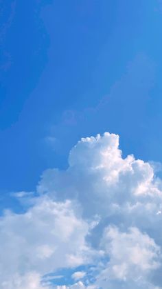 the airplane is flying high in the blue sky with fluffy white clouds above it and below