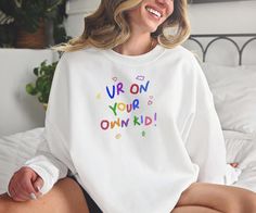 a woman sitting on a bed wearing a white sweatshirt that says love me to the moon and back