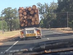 a truck with logs on the back driving down a road in front of some trees