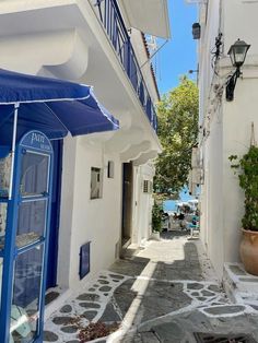 an alley way with white buildings and blue awnings on both sides that lead to the water