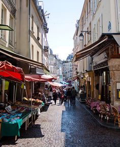 people are walking down an alley way with umbrellas on either side and tables in the middle