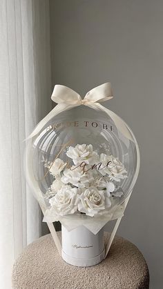 a bouquet of white flowers in a clear vase on top of a round table with the words bride to be printed on it