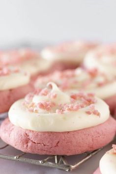 pink cookies with white frosting and sprinkles on a wire cooling rack