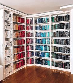 a room filled with lots of books on top of white shelving units next to a wooden floor