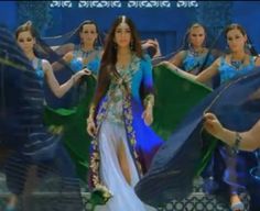 a woman in a blue and green dress is dancing with other women wearing matching outfits