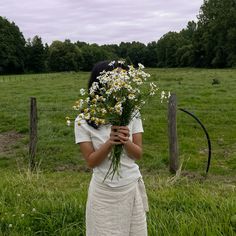 a woman holding a bunch of flowers in front of her face while standing next to a fence