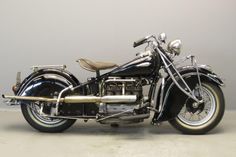 an old black motorcycle parked in a room next to a gray wall and white floor