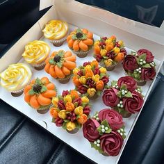 cupcakes decorated with flowers and leaves are in a box on a car seat