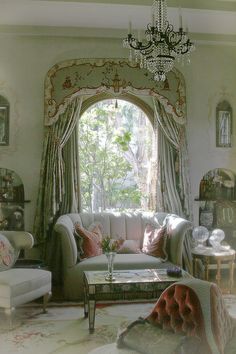 a living room filled with furniture and a chandelier hanging from the ceiling over a window