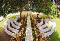 an outdoor ceremony setup with white chairs and flowers on the aisle, surrounded by trees