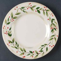 a white plate with red berries and green leaves on the rim is sitting on a gray surface