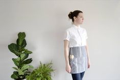 a woman standing in front of a potted plant and wearing an apron with buttons on it